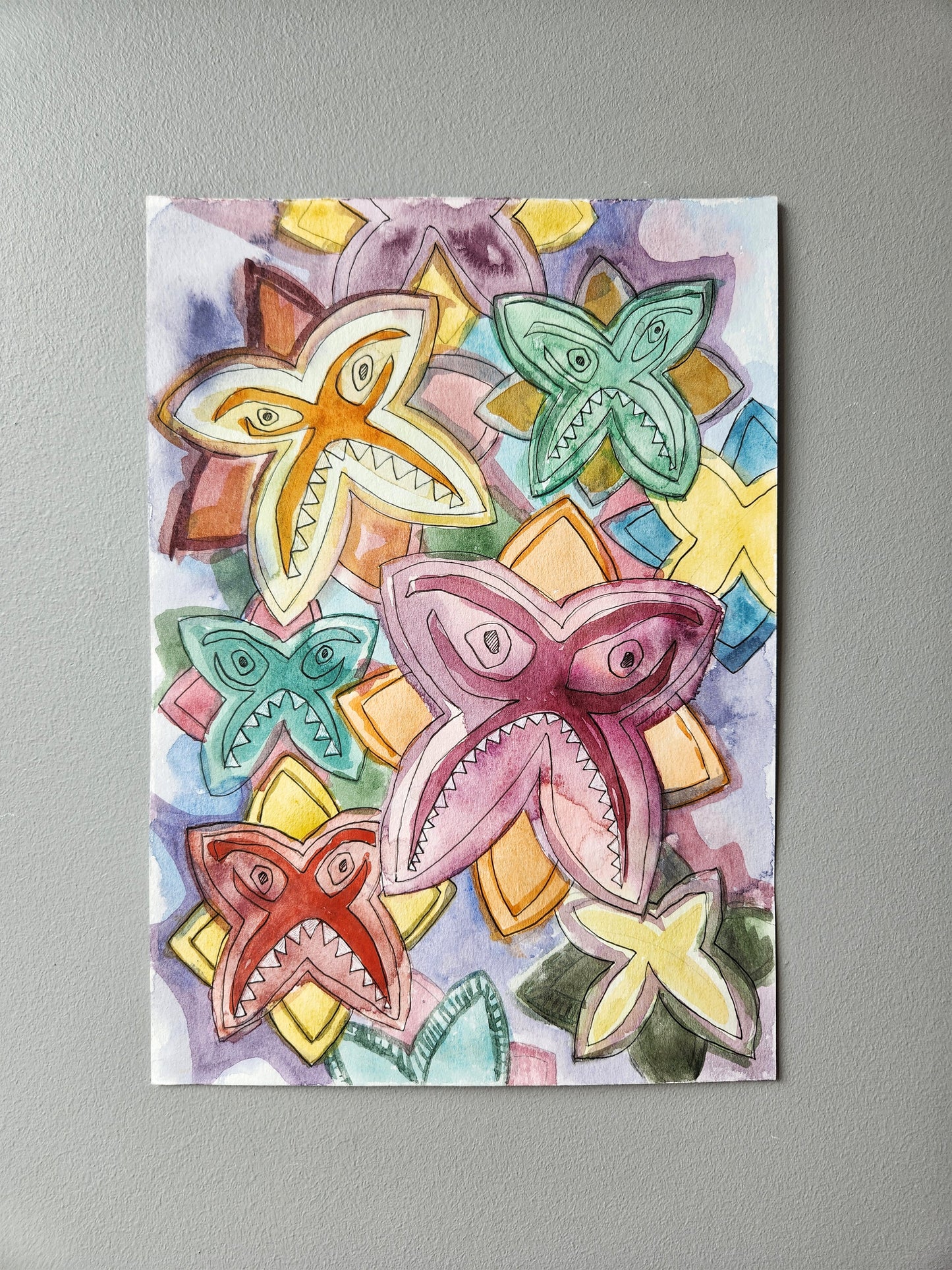 Hand-painted surreal artwork featuring colorful, flower-like creatures with sharp teeth layered over geometric star patterns; created with watercolor on paper, blending playful and eerie motifs.