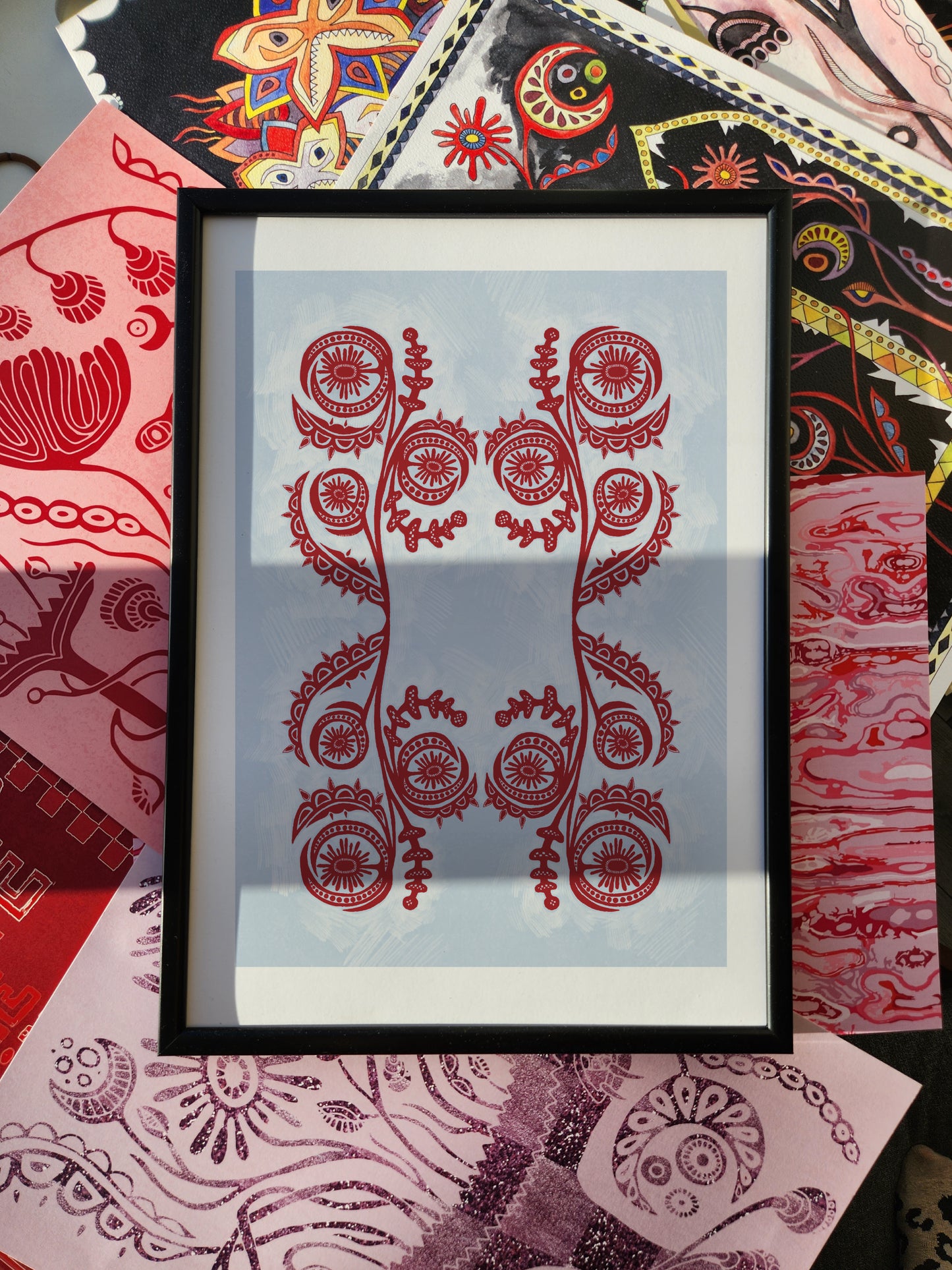 Abstract wall art poster print with red floral-inspired design, framed and displayed against a colorful eclectic patterned fabric background.