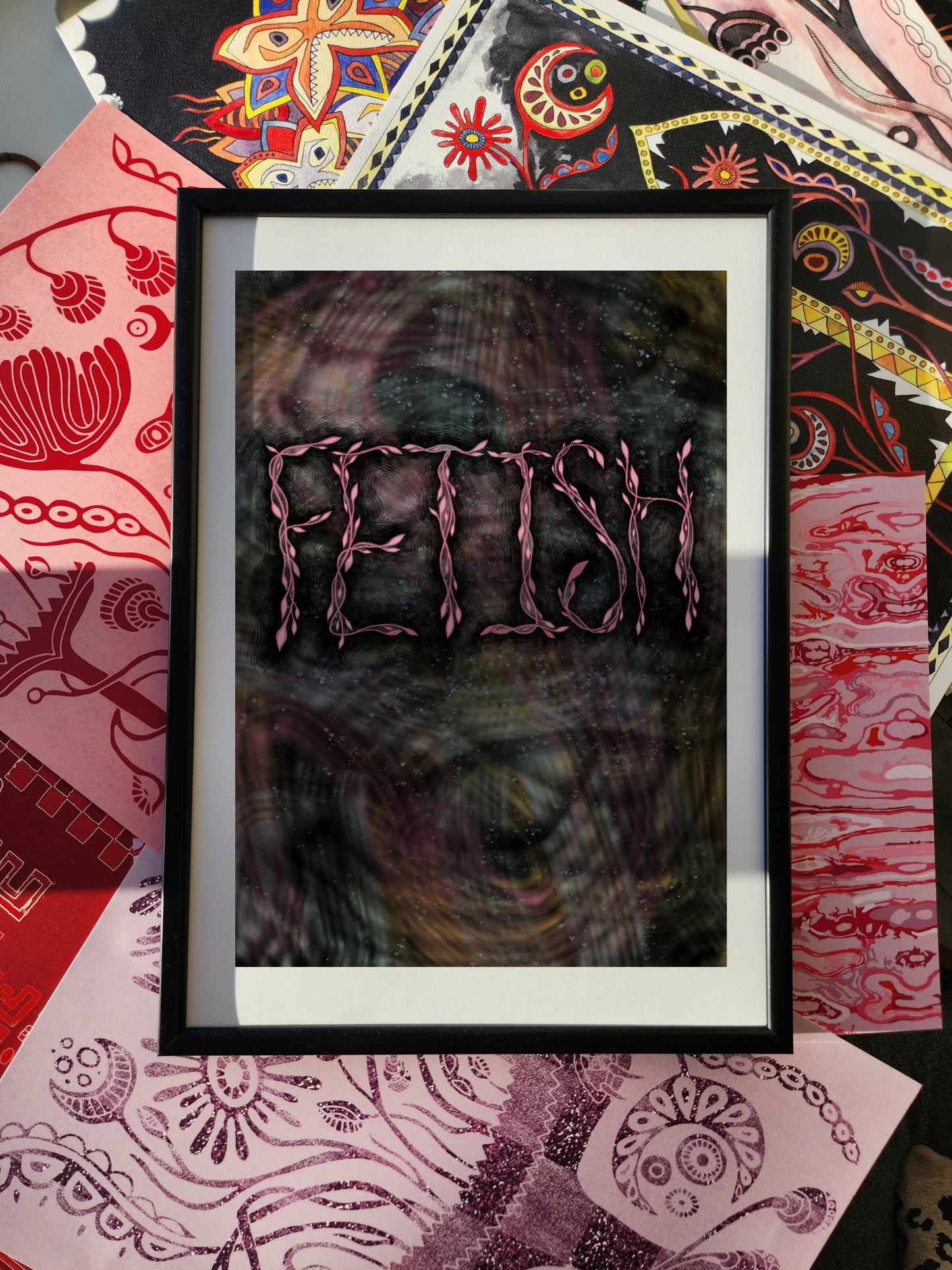 Edgy grunge wall art poster with bold typography print reading “FETISH,” framed and set against a colorful eclectic patterned fabric background.
