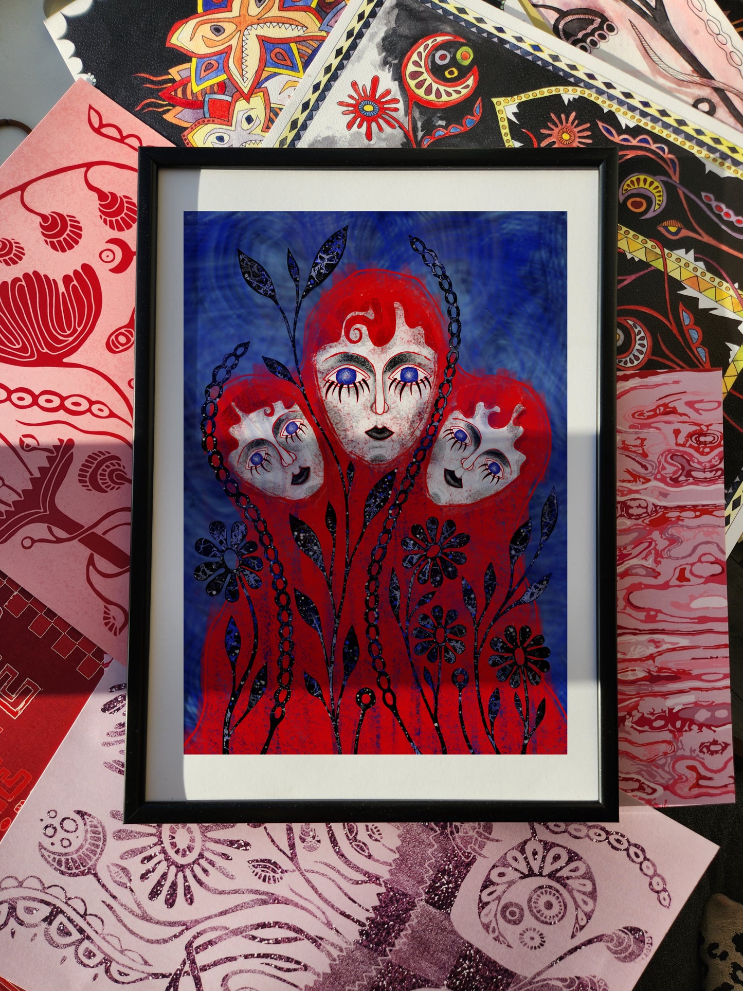 Fantasy wall art print and surreal portrait poster featuring three red-hooded faces entwined with black floral patterns on a vivid blue background.