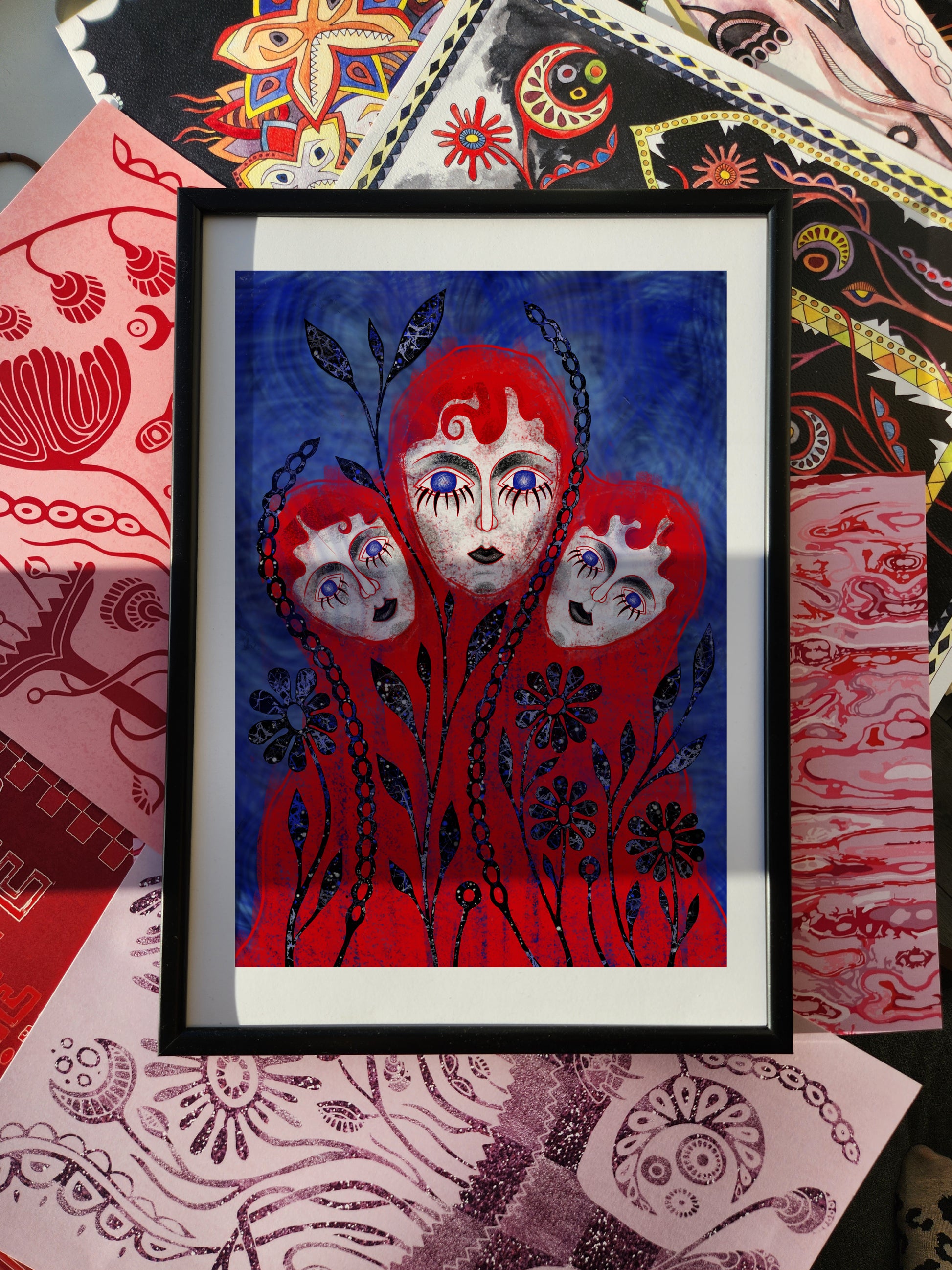 Fantasy wall art print and surreal portrait poster featuring three red-hooded faces entwined with black floral patterns on a vivid blue background.