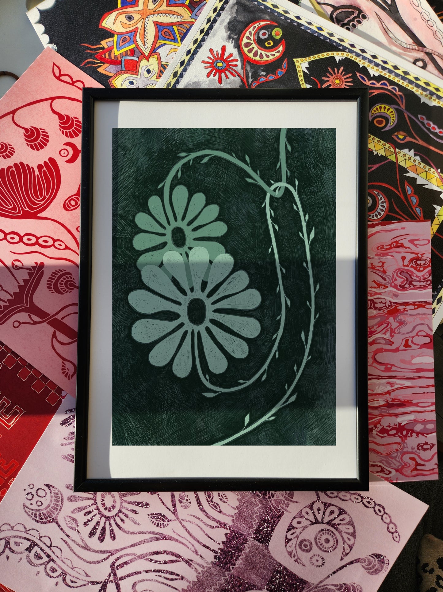 Botanical poster and floral wall art print featuring minimalist daisy-like flowers in soft green tones, framed against a bold eclectic patterned background.